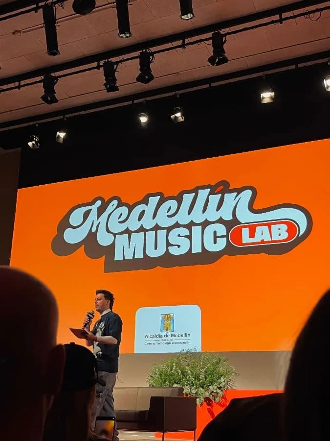 Presentación de Medellín Music Lab en un escenario con pantalla naranja